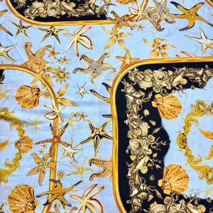 May include: A blue fabric featuring a repeating pattern of gold starfish, seashells, and ornate frames. The fabric has a luxurious and elegant feel.