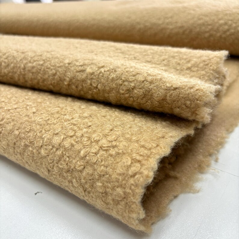 May include: Close-up of a beige, fluffy fabric with a textured surface. The fabric is folded in layers, showing the soft, plush texture.