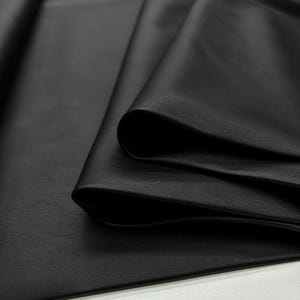 May include: Close-up of black leather fabric folded in layers. The leather has a smooth, textured surface.