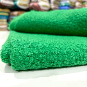 May include: A close-up of a green, fluffy fabric with a textured surface. The fabric is folded in half and the texture is visible on both sides.