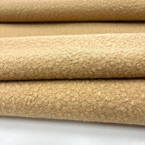 May include: Close-up of a beige fabric with a textured, fuzzy surface. The fabric is folded in thirds, showing the texture from different angles.