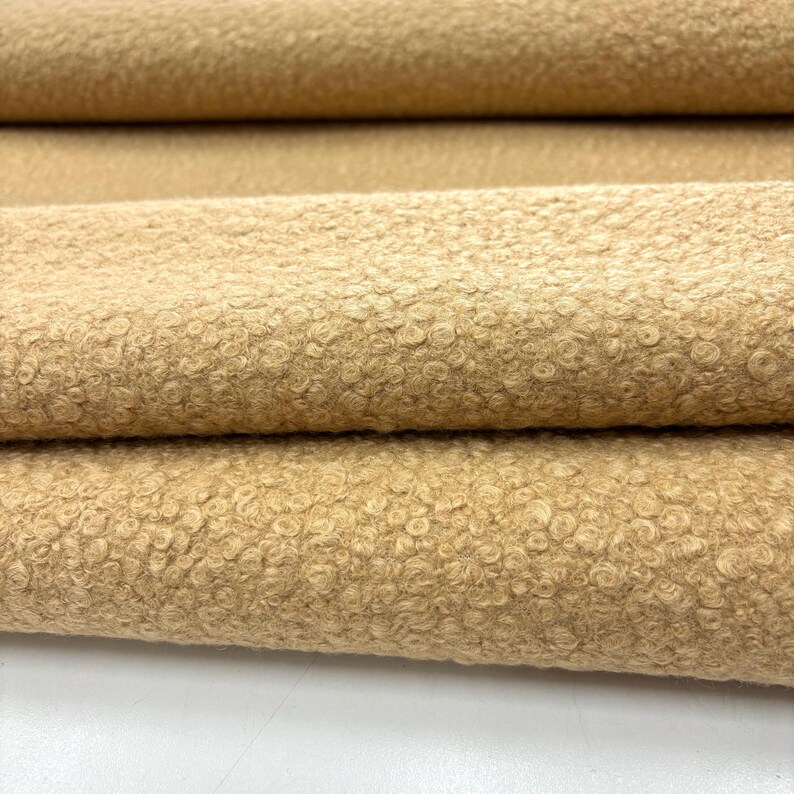 May include: Close-up of a beige fabric with a textured, fuzzy surface. The fabric is folded in thirds, showing the texture from different angles.