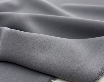 May include: Close-up of a soft, gray fabric with a textured surface. The fabric is folded and draped, showing its smooth and flowing texture.