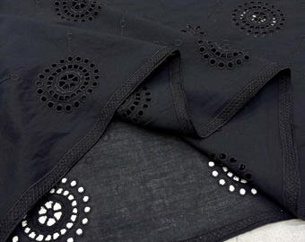 May include: Black fabric with intricate eyelet embroidery. The fabric features circular and floral patterns, with a scalloped edge. The eyelet details are evenly spaced across the material, creating a delicate and textured appearance. The fabric is folded, showing the underside.