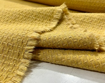 May include: Close-up of a yellow textured fabric with a frayed edge. The fabric has a waffle-like texture.