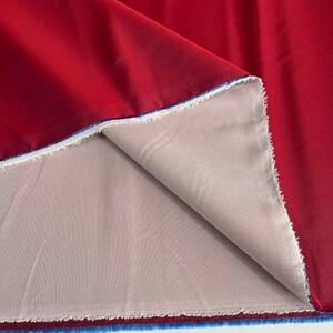 May include: Red fabric with a smooth, satin-like finish. The fabric is folded to reveal a light grey lining.