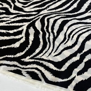 Pode incluir: Tecido de estampa de zebra preto e branco com uma borda de franja branca.