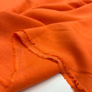 Könnte beinhalten: Nahaufnahme eines leuchtend orangefarbenen Stoffes mit einer rohen Kante. Der Stoff hat eine weiche, leicht strukturierte Oberfläche.
