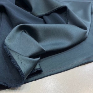 Può includere: Primo piano di un tessuto blu scuro con una finitura liscia e satinata. Il tessuto è piegato e ha un bordo grezzo.