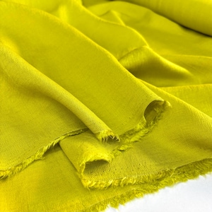 Puede incluir: Primer plano de una tela de color chartreuse vibrante, con un aspecto suave y texturizado. La tela está drapeada en pliegues fluidos, con bordes deshilachados visibles. El material parece ligero y adecuado para ropa o decoración del hogar.