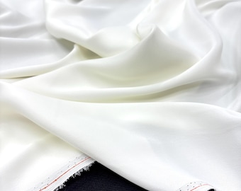 Puede incluir: Tela blanca con una textura suave y sedosa. La tela está doblada y drapeada, mostrando su naturaleza suave y fluida. Los bordes de la tela están acabados con una costura roja.
