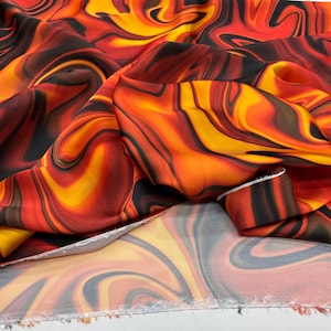 May include: A colourful fabric featuring a swirling pattern in red, orange, yellow, and black. The design evokes flowing lava or flames. The fabric is folded, revealing the raw edge of the material.