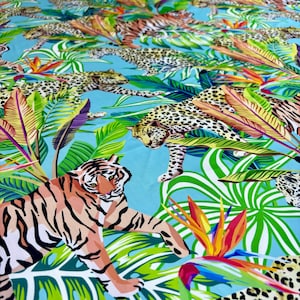 May include: A blue fabric with a repeating pattern of tigers and leopards in a jungle setting. The animals are depicted in a colourful, stylised design with green, yellow, orange, and red accents.