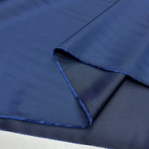 May include: A close-up of a dark blue fabric with a smooth, silky texture. The fabric is folded in half, revealing the underside.