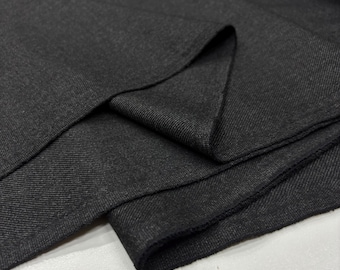 Puede incluir: Primer plano de una tela gris oscuro doblada. La tela tiene una apariencia sutil y texturizada con un ligero brillo. Los pliegues crean sombras y profundidad, resaltando la textura y las variaciones de color del material. La tela parece ser un material de peso medio.