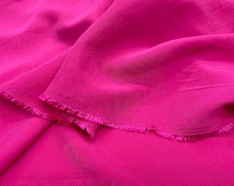 Puede incluir: Una tela de color rosa brillante con un borde festoneado. La tela es suave y fluida, y tiene un brillo sutil.