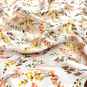 May include: White fabric with a repeating floral pattern in shades of yellow, orange, brown, and green. The design features delicate branches and leaves, creating a natural and elegant aesthetic. The fabric has a subtle sheen.