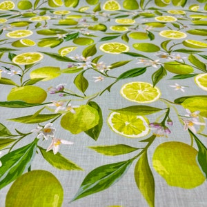 May include: Fabric with a repeating pattern of green limes, lime slices, white blossoms, and green leaves on a light blue background. The design features whole limes, sliced limes, and floral elements.