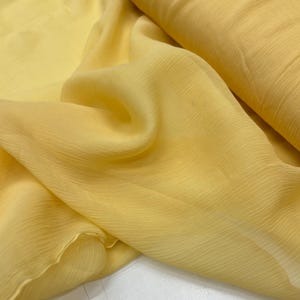 May include: A piece of yellow sheer fabric with a crinkled texture. The fabric is soft and flowing, and it has a subtle sheen.