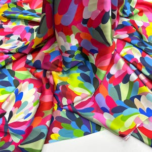 Può includere: Un tessuto colorato con un motivo floreale astratto luminoso in tonalità di rosa, rosso, blu, verde, giallo e bianco.