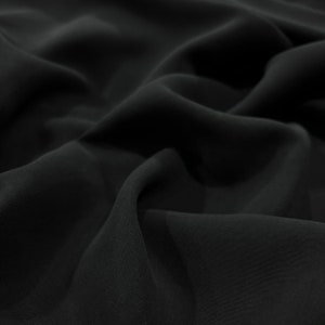 May include: Close-up of a black fabric with a smooth, silky texture. The fabric is draped and folded, creating soft, flowing lines.