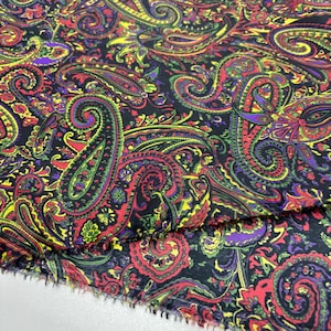 May include: Close-up of a fabric with a paisley pattern. The fabric has a black background with a repeating design of colourful paisley shapes in red, green, yellow, and purple. The edges of the fabric are unfinished.