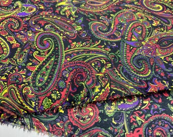 May include: Close-up of a fabric with a paisley pattern. The fabric features a black background with a repeating design of colorful paisley shapes in red, green, yellow, and purple. The edges of the fabric are unfinished.
