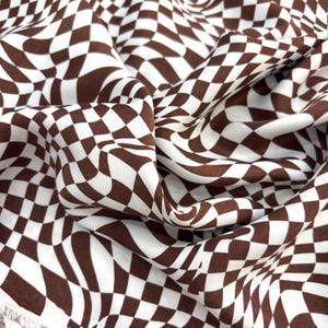 May include: Brown and white checkered fabric with a wavy pattern. The fabric is tightly woven and has a smooth texture. The pattern is a repeating grid of brown and white squares, creating a visually dynamic design.