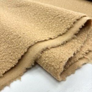 May include: Close-up of a beige, fuzzy fabric with a textured surface. The fabric is folded in half, showing the soft, plush texture.