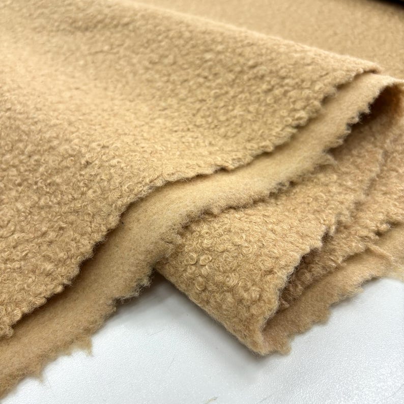 May include: Close-up of a beige, fuzzy fabric with a textured surface. The fabric is folded in half, showing the soft, plush texture.