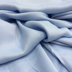 Puede incluir: Una tela azul claro con una textura suave y sedosa. La tela está doblada y drapeada, mostrando su naturaleza suave y fluida.