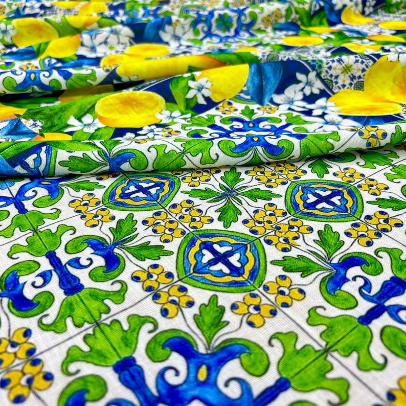 May include: White fabric with a repeating pattern of blue, green, and yellow geometric shapes. The fabric has a folded edge.