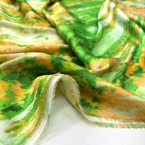 Puede incluir: Tela de estampado abstracto verde y naranja sobre fondo blanco. La tela está doblada y tiene una textura suave y sedosa.