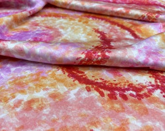 Puede incluir: Primer plano de una tela de tie-dye rosa, naranja y roja con un patrón de remolino. La tela es suave y sedosa.