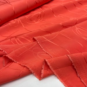 Puede incluir: Tela de color coral con un sutil patrón en relieve de líneas curvas. La tela tiene un borde sin terminar.