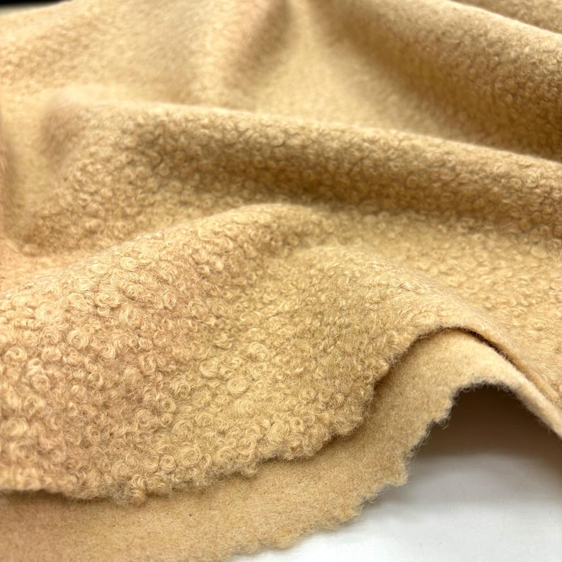 May include: A close-up of a beige, textured fabric with a soft, fuzzy surface. The fabric is folded in half, showing the smooth underside.