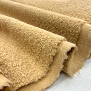 May include: Close-up of a soft, brown, fuzzy fabric with a textured surface. The fabric is folded in a way that shows the texture and the soft, fluffy feel.