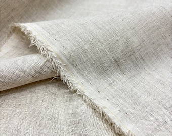 May include: Close-up of a piece of natural-colored linen fabric. The fabric has a textured weave and a raw, frayed edge. The color is a neutral beige with subtle variations in tone, suggesting a high-quality textile.