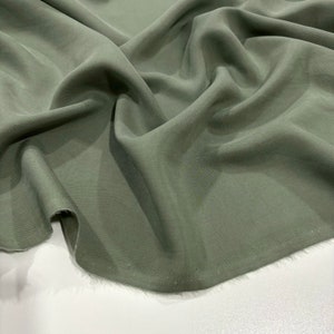 Puede incluir: Primer plano de una tela verde oliva fluida. El material está drapeado y texturizado, con pliegues y sombras suaves. La tela parece ligera y adecuada para ropa o decoración del hogar.