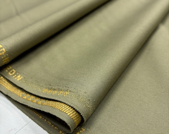 Puede incluir: Primer plano de un trozo de tela doblado de color verde con un ribete dorado. La tela tiene una textura sutil y un acabado liso.