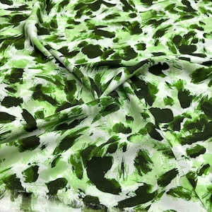 Puede incluir: Tela verde y blanca con un patrón de pinceladas. La tela tiene una textura suave y fluida.