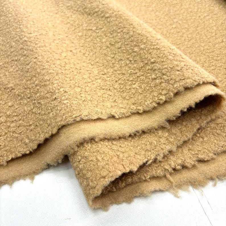 May include: Close-up of a beige, fuzzy fabric with a textured surface. The fabric is folded in half, showing the soft, plush texture.