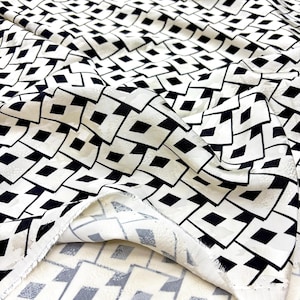 May include: White fabric featuring a repeating pattern of black diamond shapes. The fabric is folded, revealing its texture and drape. This abstract design is suitable for clothing or interior design projects.