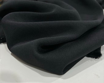May include: Close-up of a black fabric with a smooth, silky texture. The fabric is folded and draped, showcasing its soft and flowing nature.