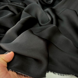 May include: Black satin fabric with a smooth, silky texture. The fabric is draped and folded, showcasing its luxurious feel.