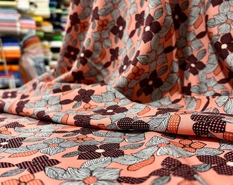 May include: Peach-colored fabric with a floral pattern. The flowers are a mix of white, orange, and brown. The fabric has a textured surface.