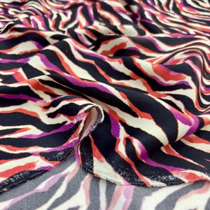 May include: A close-up of fabric with a striking zebra stripe design. The pattern incorporates black, white, red, and purple stripes. The fabric is folded, revealing its texture and drape. Suitable for clothing and interior design projects.