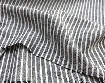 May include: Close-up of a fabric with a black and white striped pattern. The fabric has vertical stripes of varying widths. The edges of the fabric are frayed, adding a textured detail. The fabric appears to be linen or a similar material.