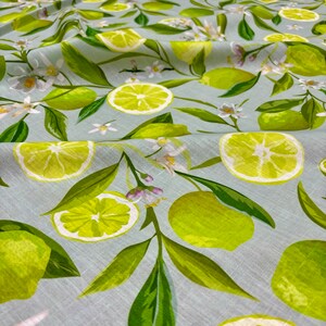 May include: Fabric with a light blue background featuring a pattern of green limes, lime slices, green leaves, and white blossoms. The limes are whole and sliced, with a watercolor style. The fabric is suitable for various sewing projects.
