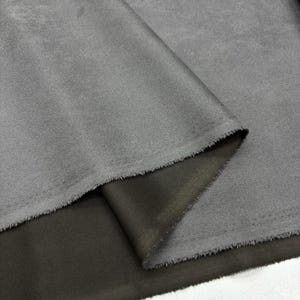 Puede incluir: Primer plano de una tela gris con una textura lisa y sedosa. La tela está doblada, revelando un lado inferior gris más oscuro.